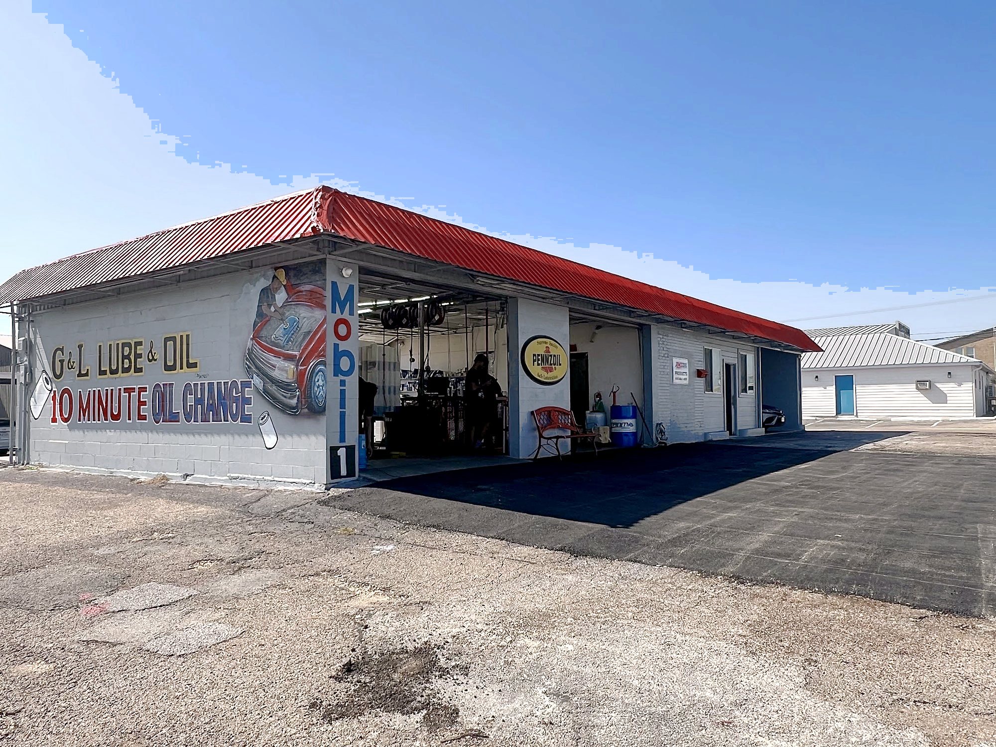 G&L Lube & Oil: a light gray block building with a red metal roof, the bay door open, and the hand-painted mural on the side wall