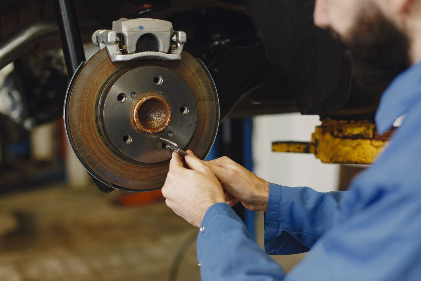 Hands working on a brake caliper and rotor with the wheel off